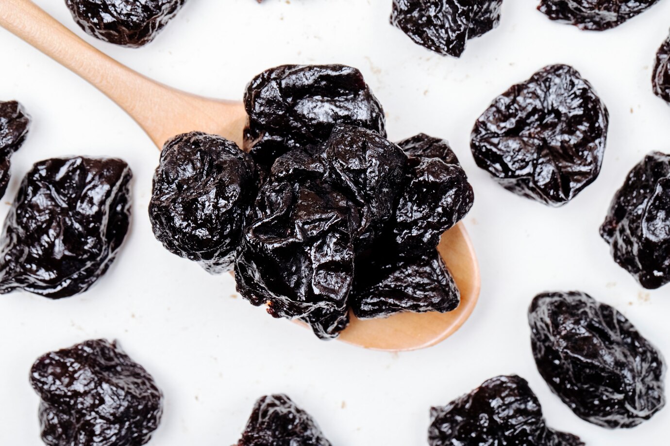 top-view-wooden-spoon-with-dried-plums-prunes-white-background_141793-9340
